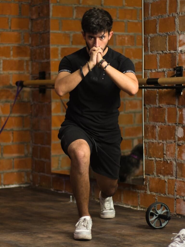 A young man in a black shirt stretching indoors against a brick wall.