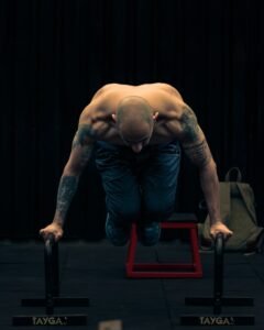 Muscular man performing calisthenics on parallettes in a Mexico City gym.