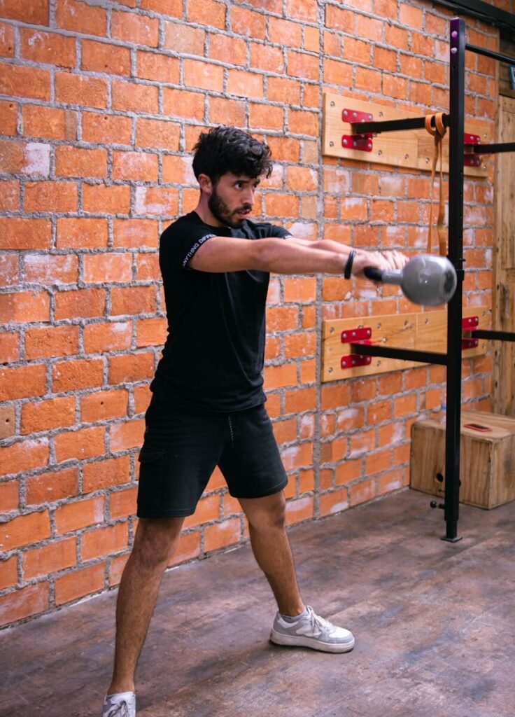 Young man performing kettlebell swings indoors against a brick wall.