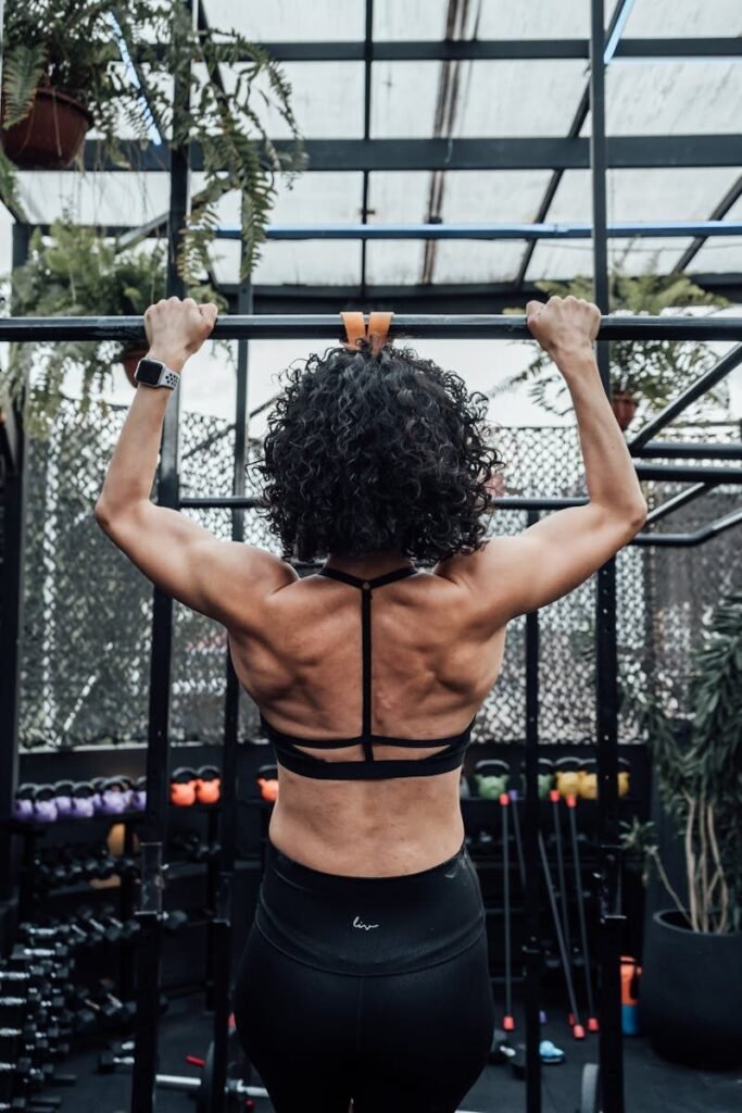 Rear view of a woman working out with pull-ups in a gym, showcasing strength and fitness.